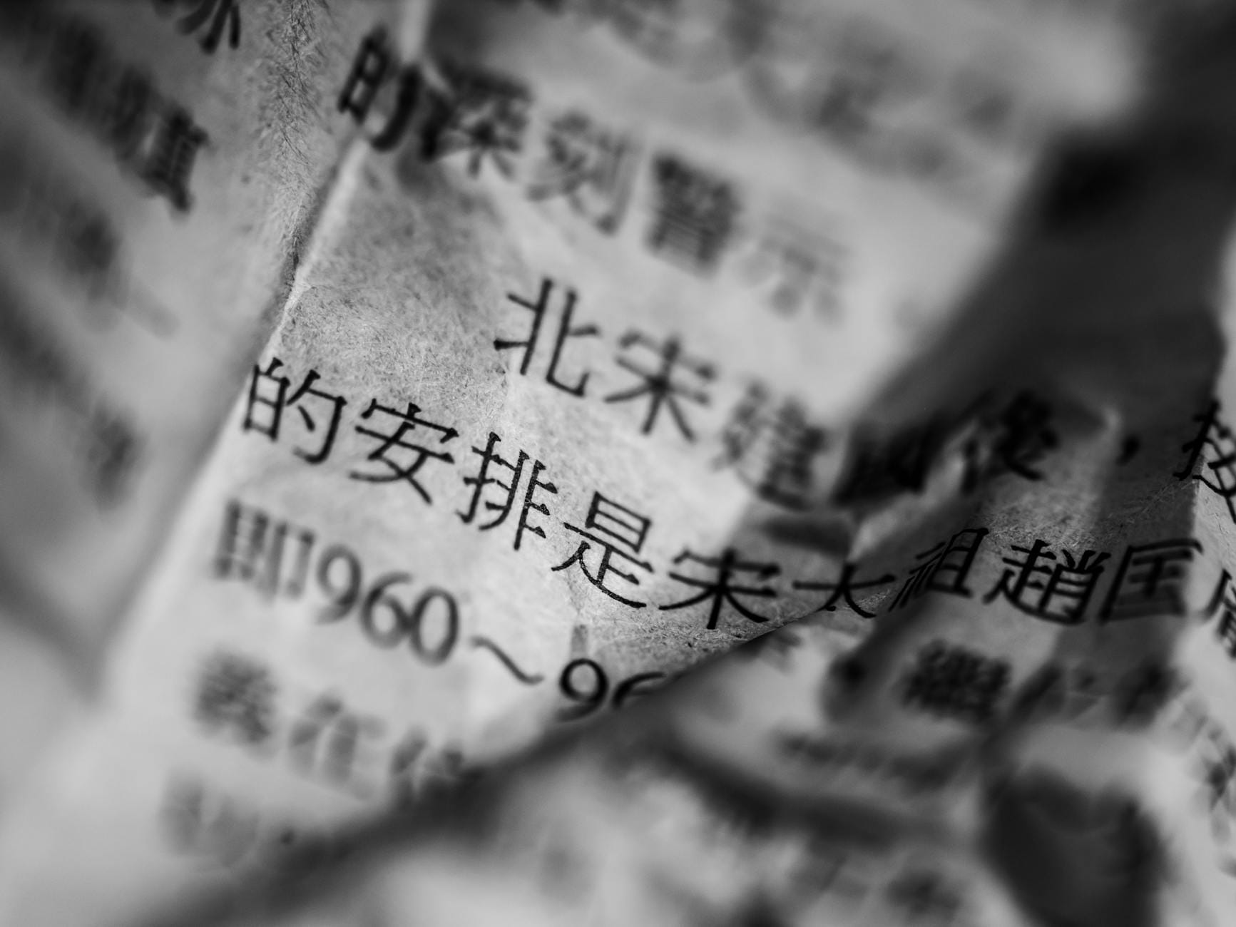 Black and white close-up of crumpled Chinese newspaper with selective focus on text.